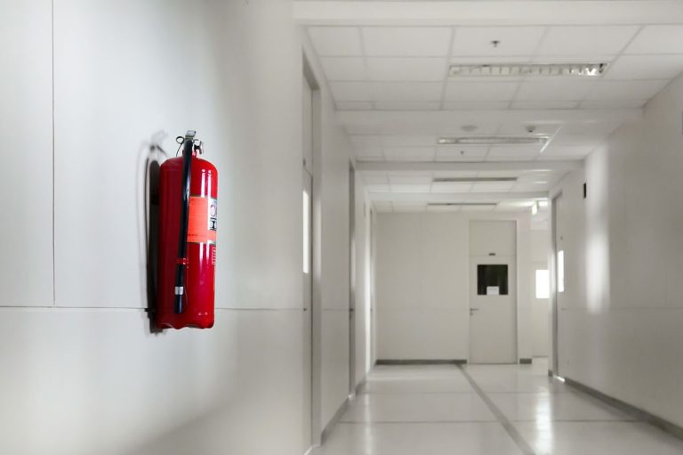 Brandschutzbeauftragter health & safety ehrl Ein roter Feuerlöscher hängt gut sichtbar an der Wand eines weißen Flures.