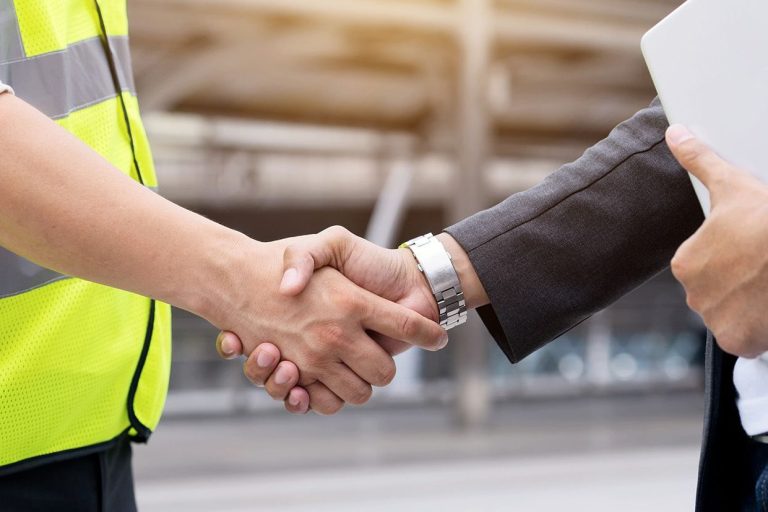 Sicherheitstechnische Betreuung health & safety ehrl Händeschütteln zwischen einem Geschäftsmann und einem Mitarbeiter in Arbeitskleidung.